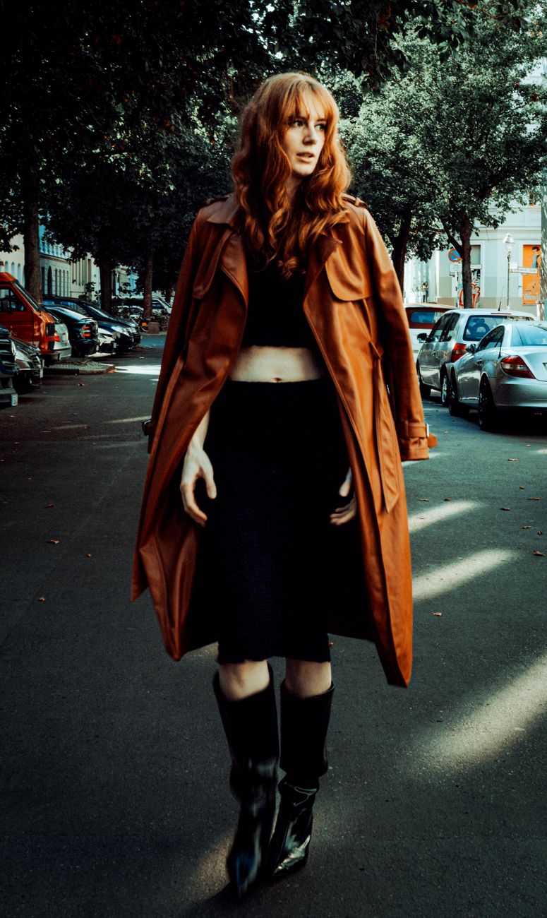 Fashionable woman in trench coat strolls down a Berlin street, exuding urban style.