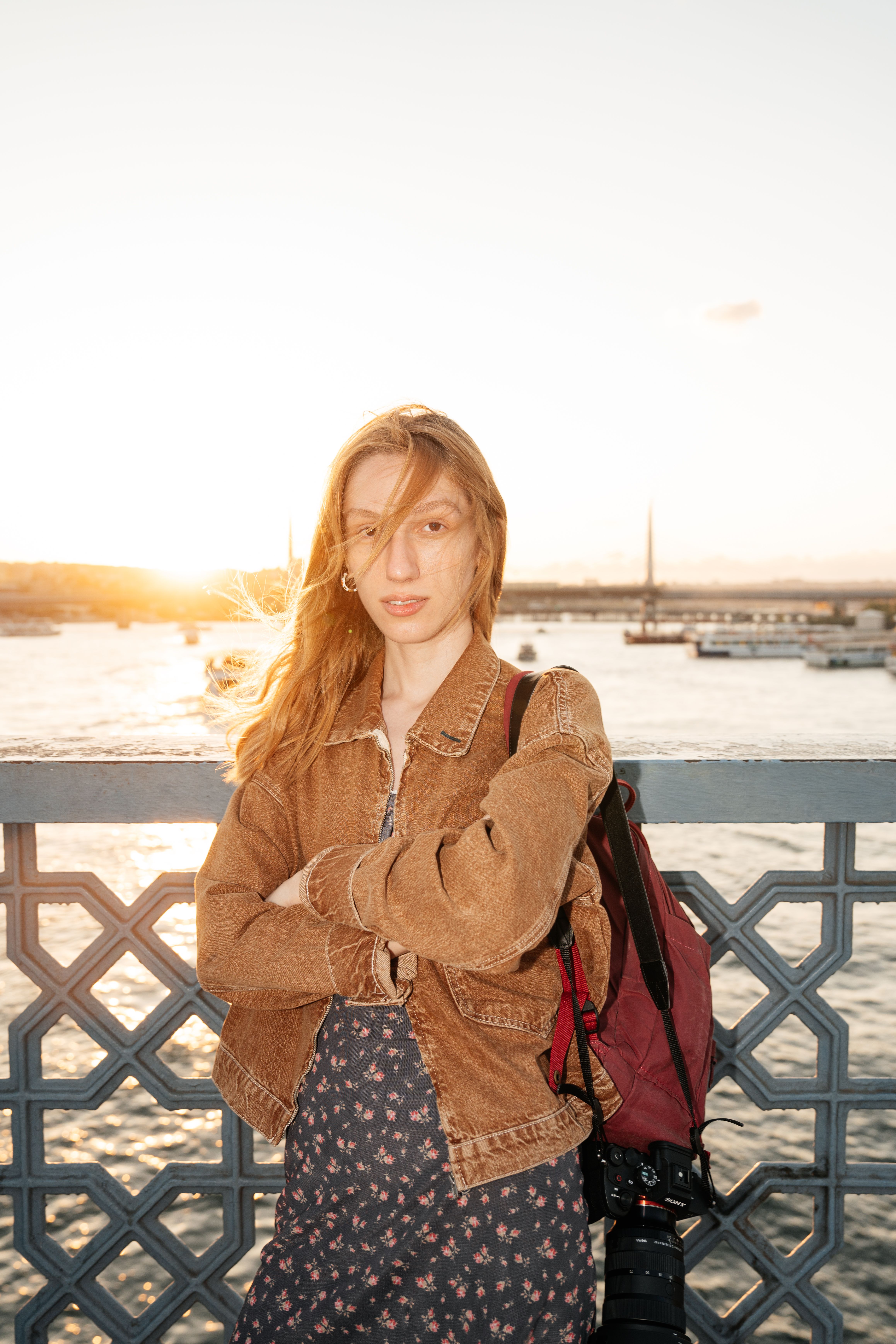 A young woman stands on Galata Bridge in İstanbul at sunset, capturing a serene urban moment.