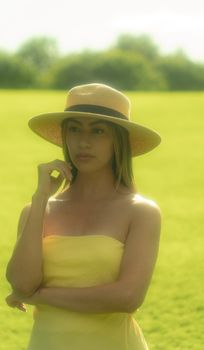 A serene portrait of a woman in a yellow dress and sun hat standing in a sunlit field.