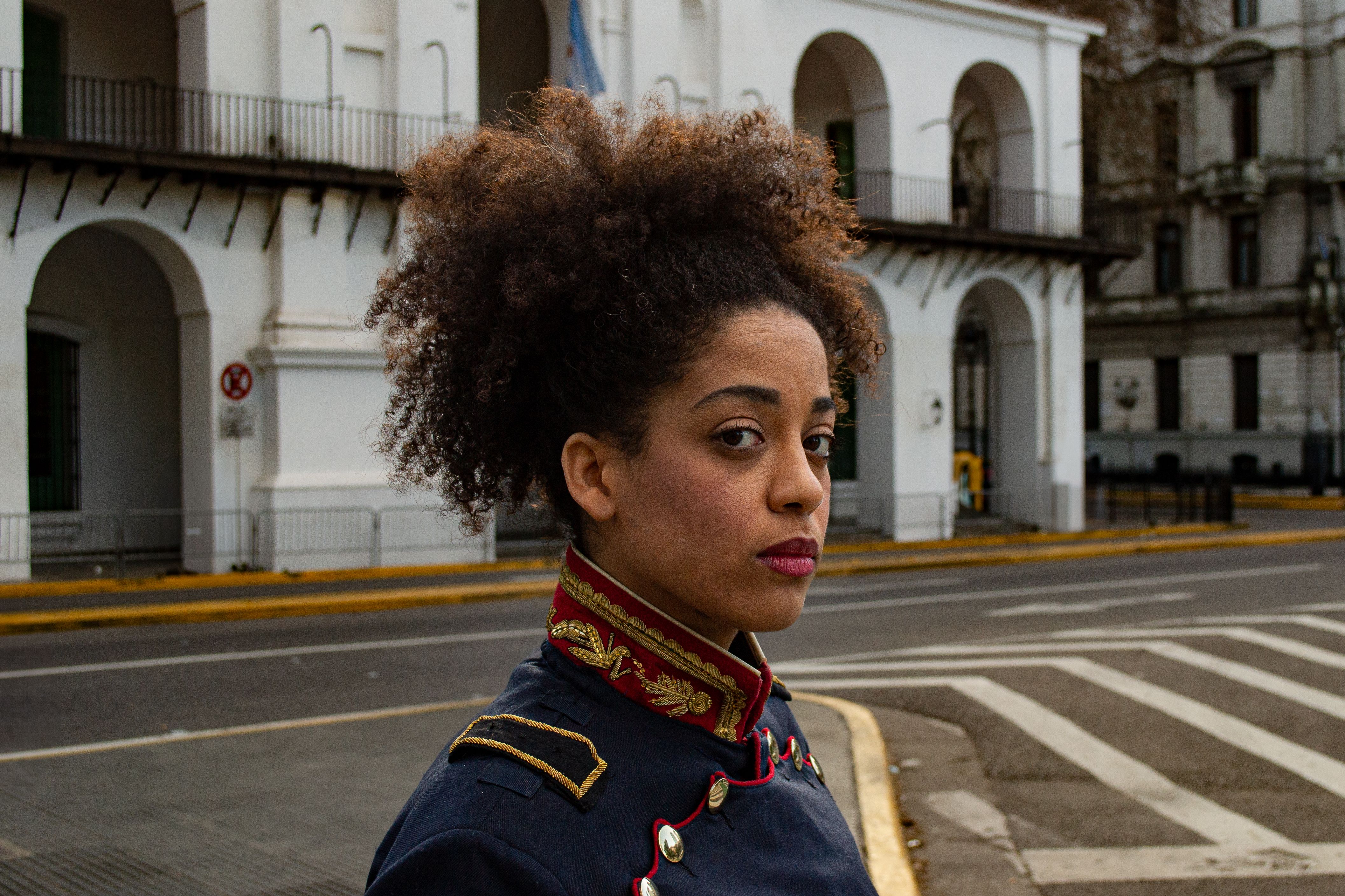 Woman in traditional attire stands confidently at a historic site in Buenos Aires.