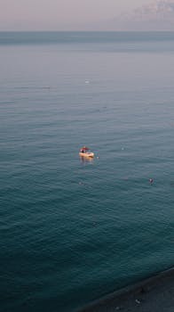 A lone boat floats on the tranquil sea, framed by distant mountains at dusk.