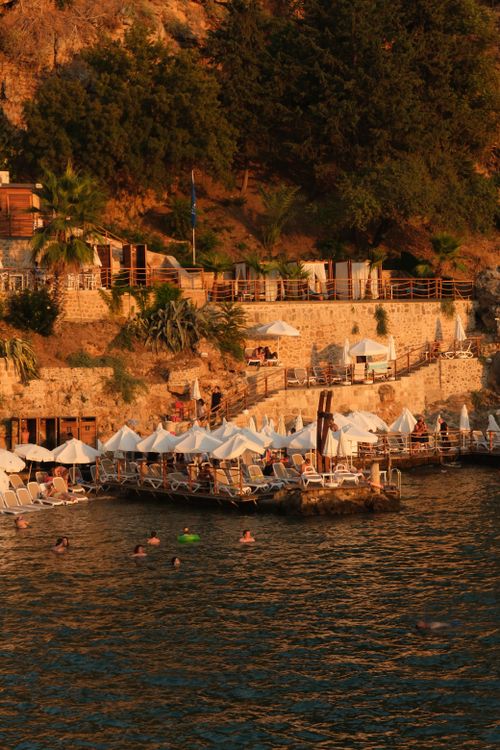 Free Cliffside beach resort with umbrellas and swimmers during sunset. Serene summer vibe. Stock Photo