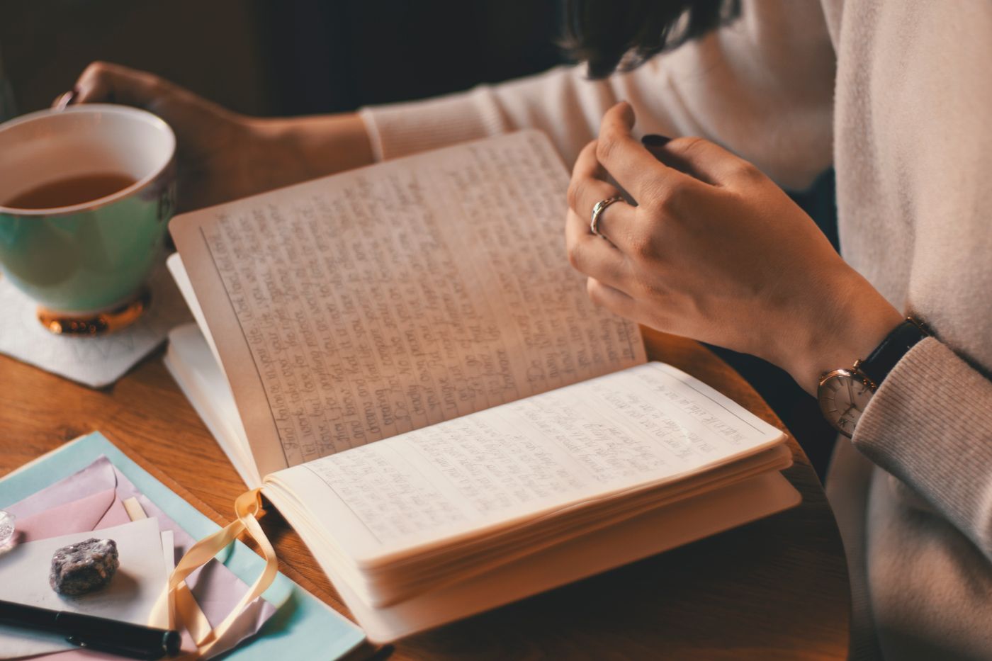 Mujer escribiendo en un cuaderno junto a una taza, mesa de madera y luz de ventana, sin mirar a cámara