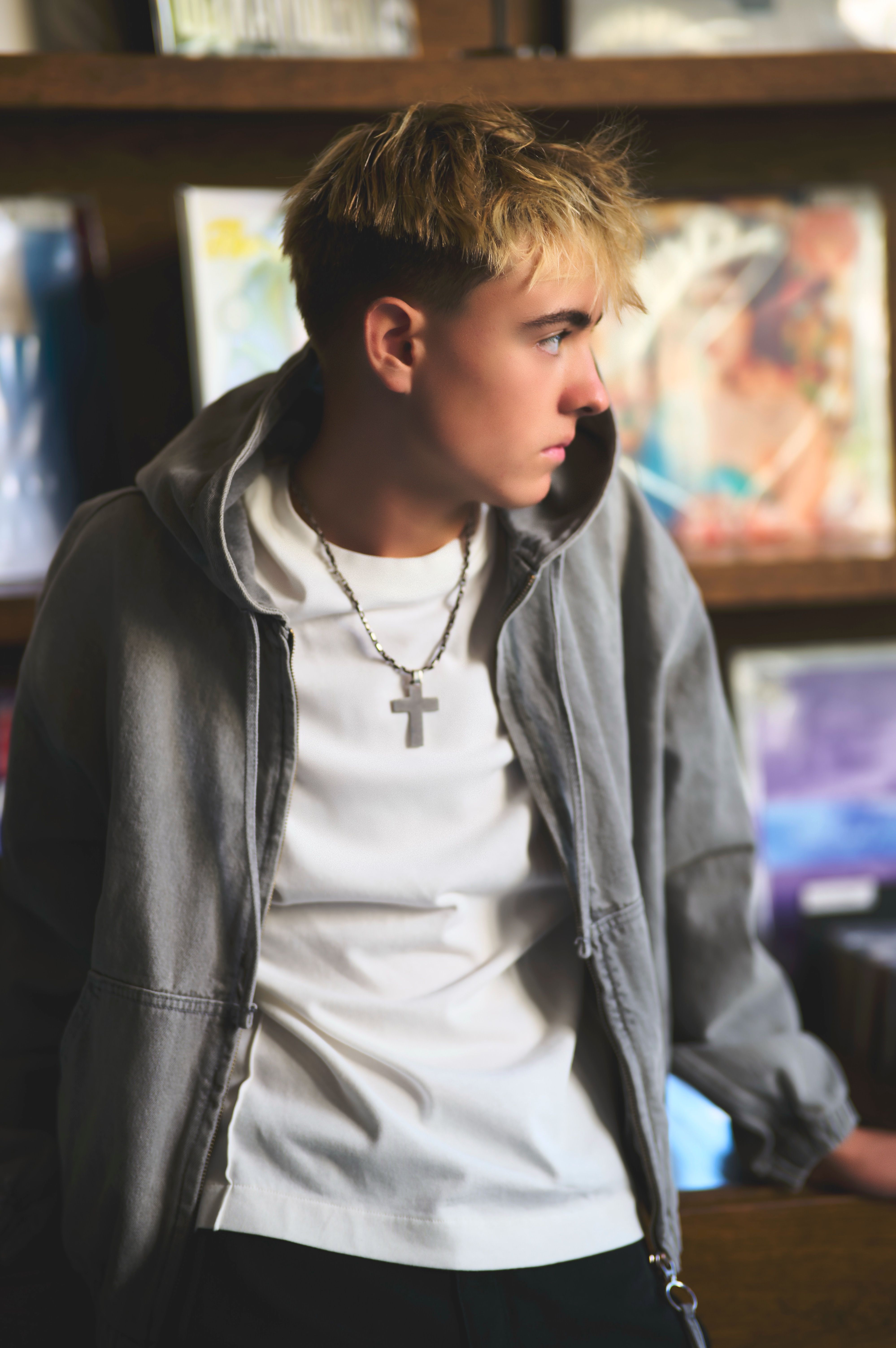 A stylish young man in casual wear with cross necklace in an urban record store, looking to the side.