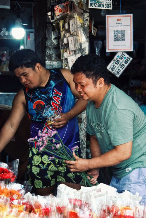 Free Two men arranging and selling flowers at a busy indoor market stall. Stock Photo