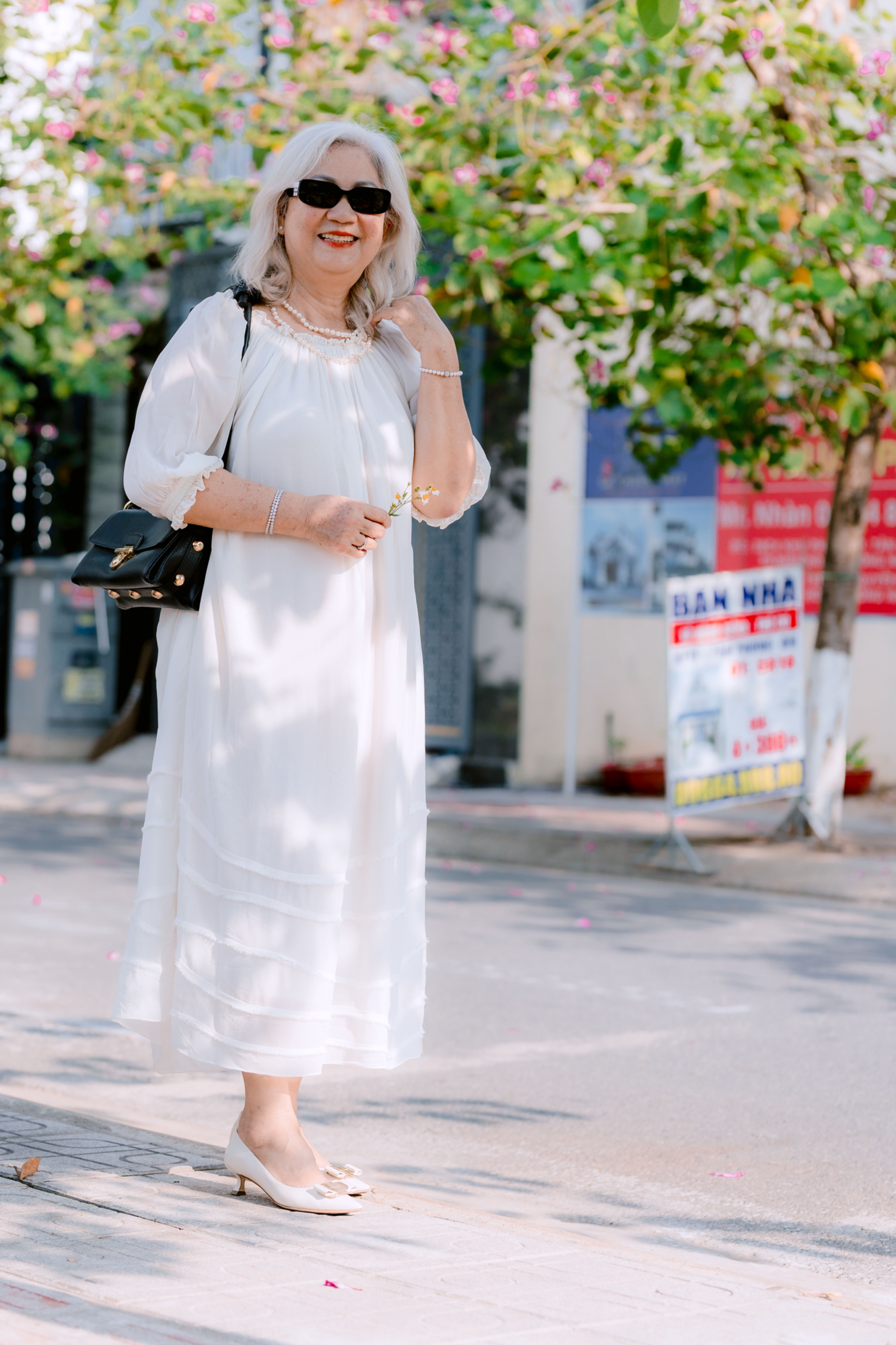 Senior woman wearing a loose white midi dress outdoors on a sunny day