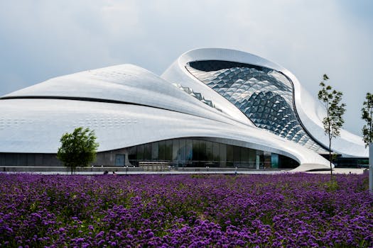 Striking modern architecture with an expansive field of purple flowers in the foreground under a cloudy sky.