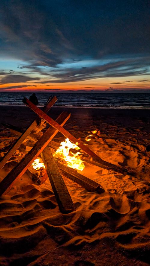 Free A tranquil beach bonfire burns bright at sunset, offering warm light as the sky darkens. Stock Photo