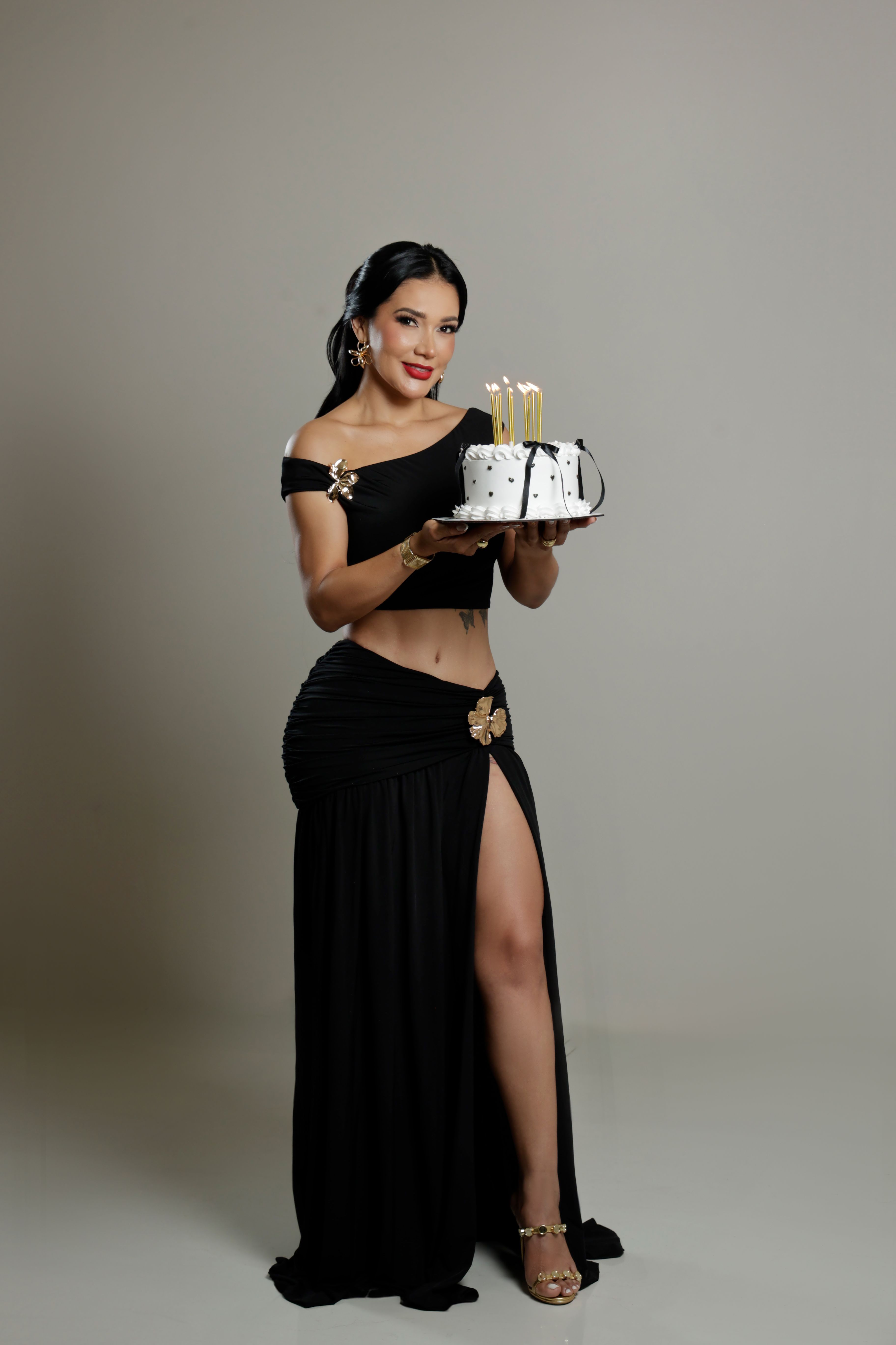 Elegant woman in a black dress holds a cake with candles in Santo Domingo studio.