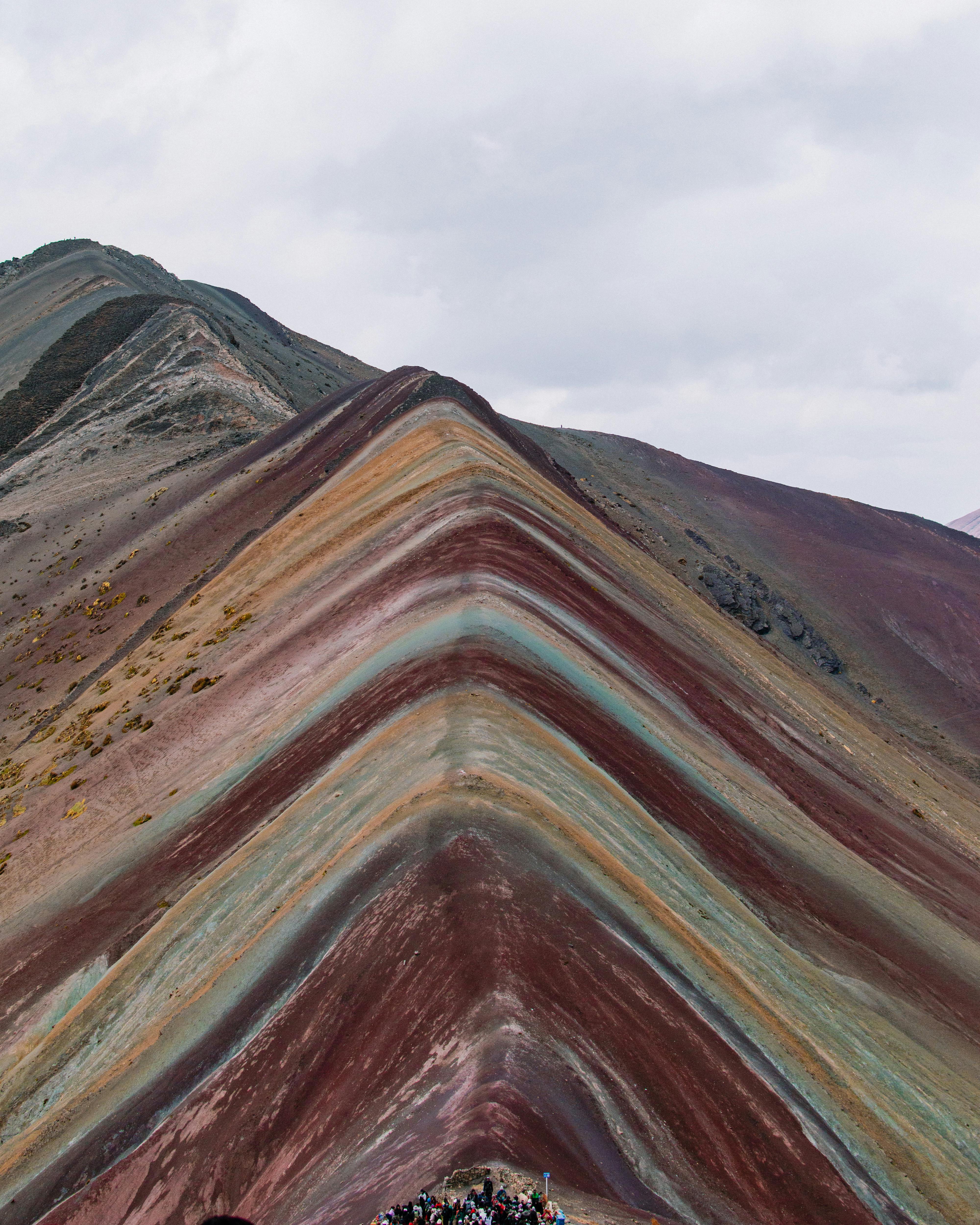 A breathtaking view of Rainbow Mountain in the Peruvian Andes, showcasing its vibrant layered colors against a cloudy sky.