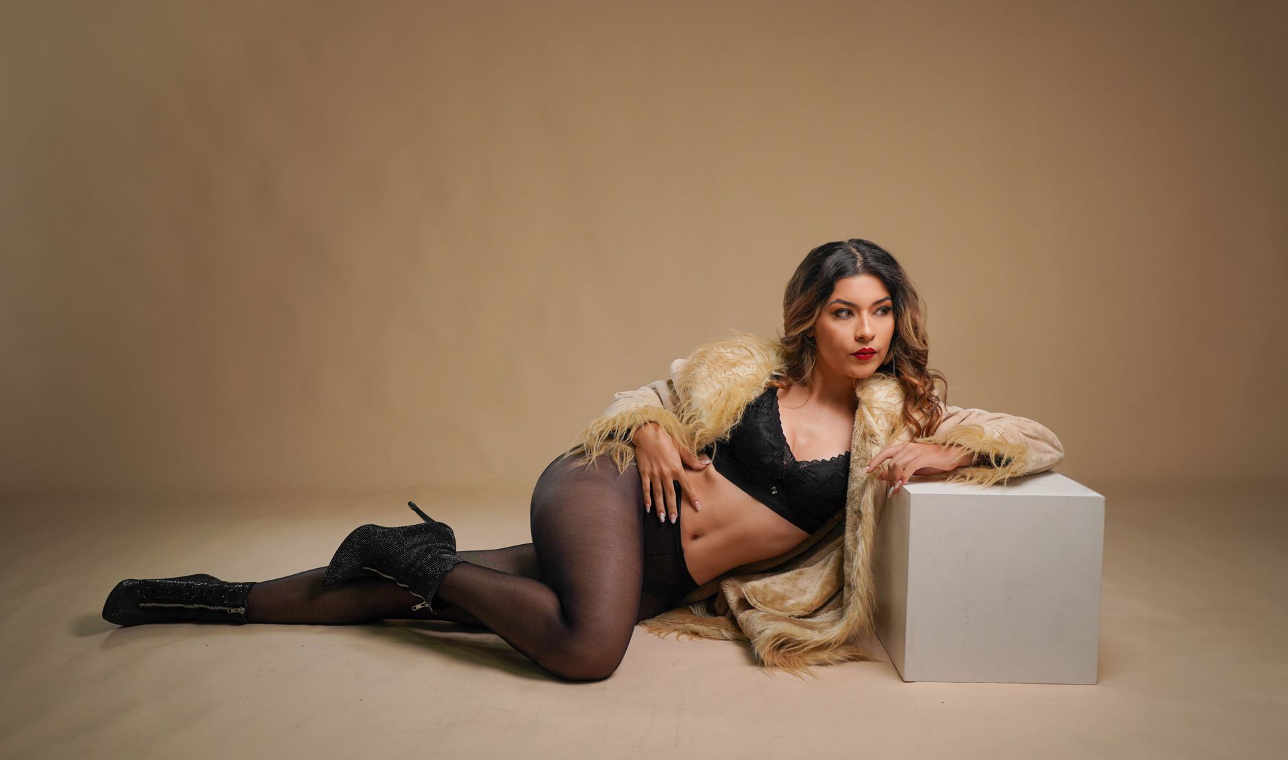 Stylish woman in lingerie and fur coat posing in a studio environment.