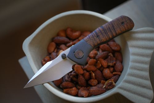 Free A sleek pocket knife lies on top of a bowl filled with almonds, showcasing its refined design. Stock Photo