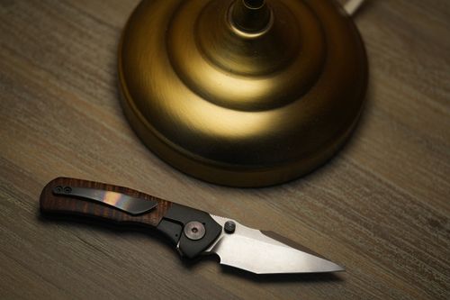 Free Close-up of an elegant folding pocket knife beside a golden lamp base on a wooden surface. Stock Photo