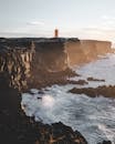 日落时分，冰岛崎岖海岸线上灯塔的壮丽景色，展示了引人注目的悬崖和海浪