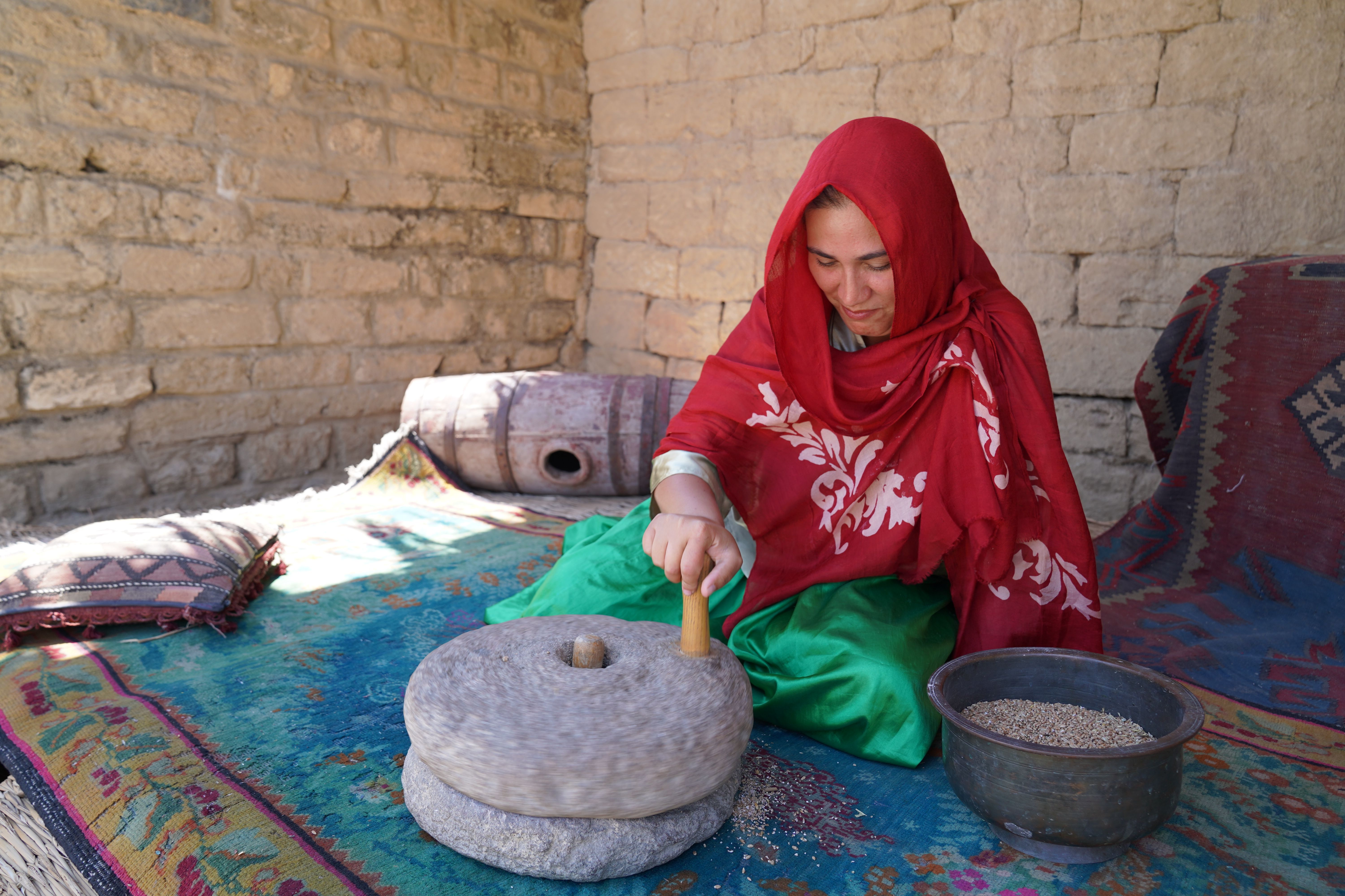 Woman in red headscarf using stone grinder indoors, showcasing cultural heritage.