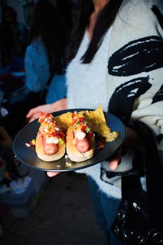 Plate of gourmet hot dogs topped with salsa served with tortilla chips at an outdoor gathering.