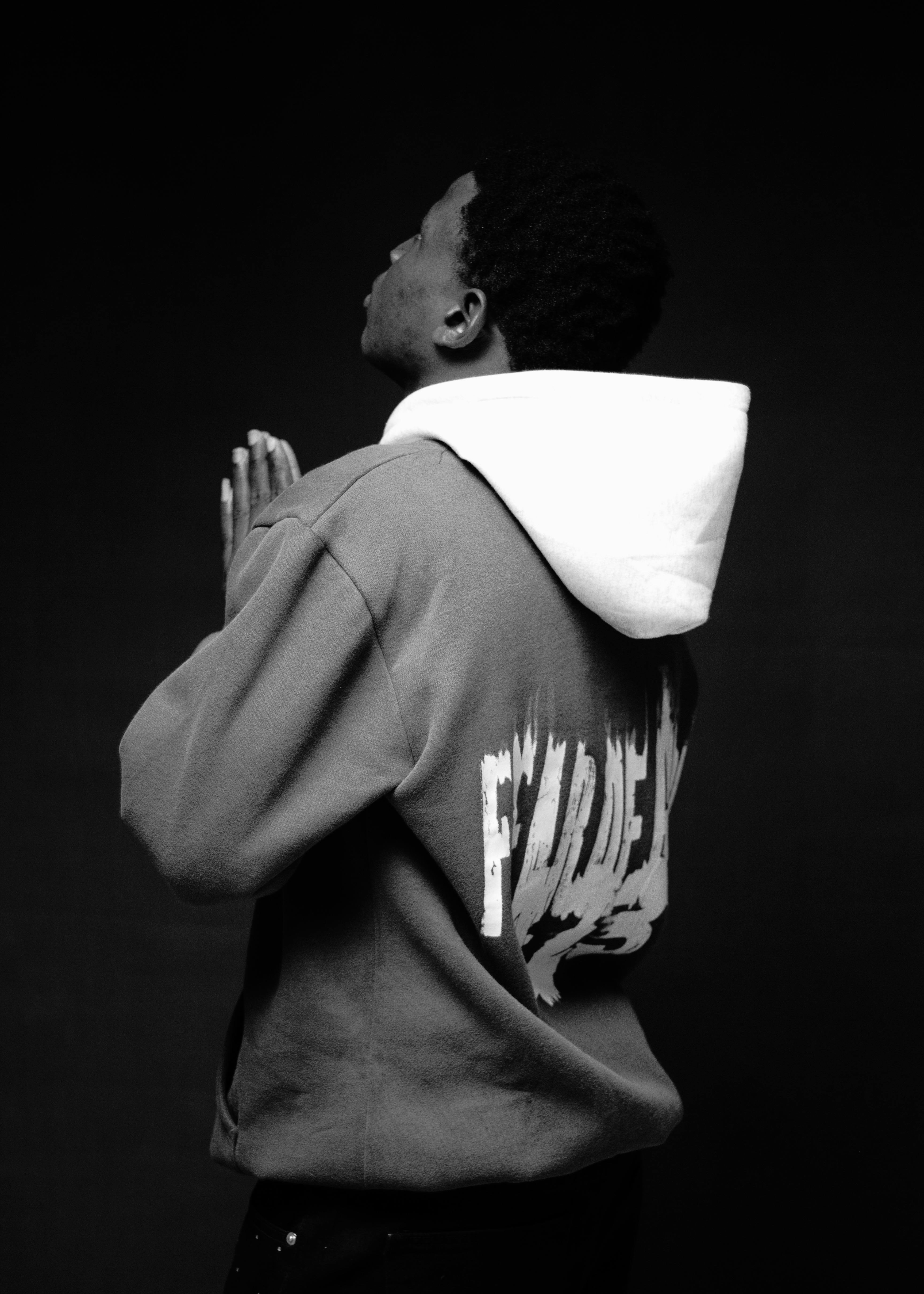 Black and white photo of a young man in a hoodie praying.