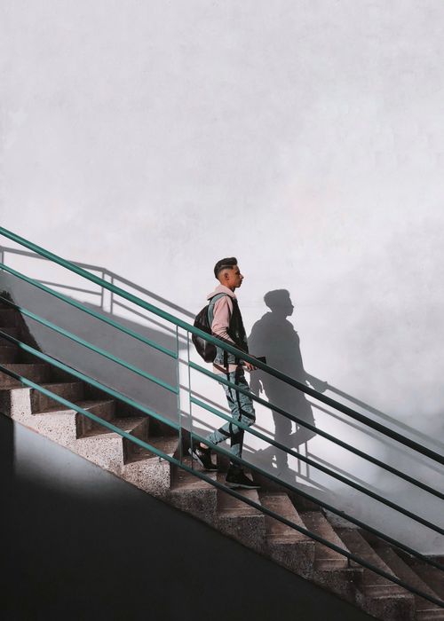 Free Man with backpack descending an outdoor staircase casting a shadow on a sunny day. Stock Photo