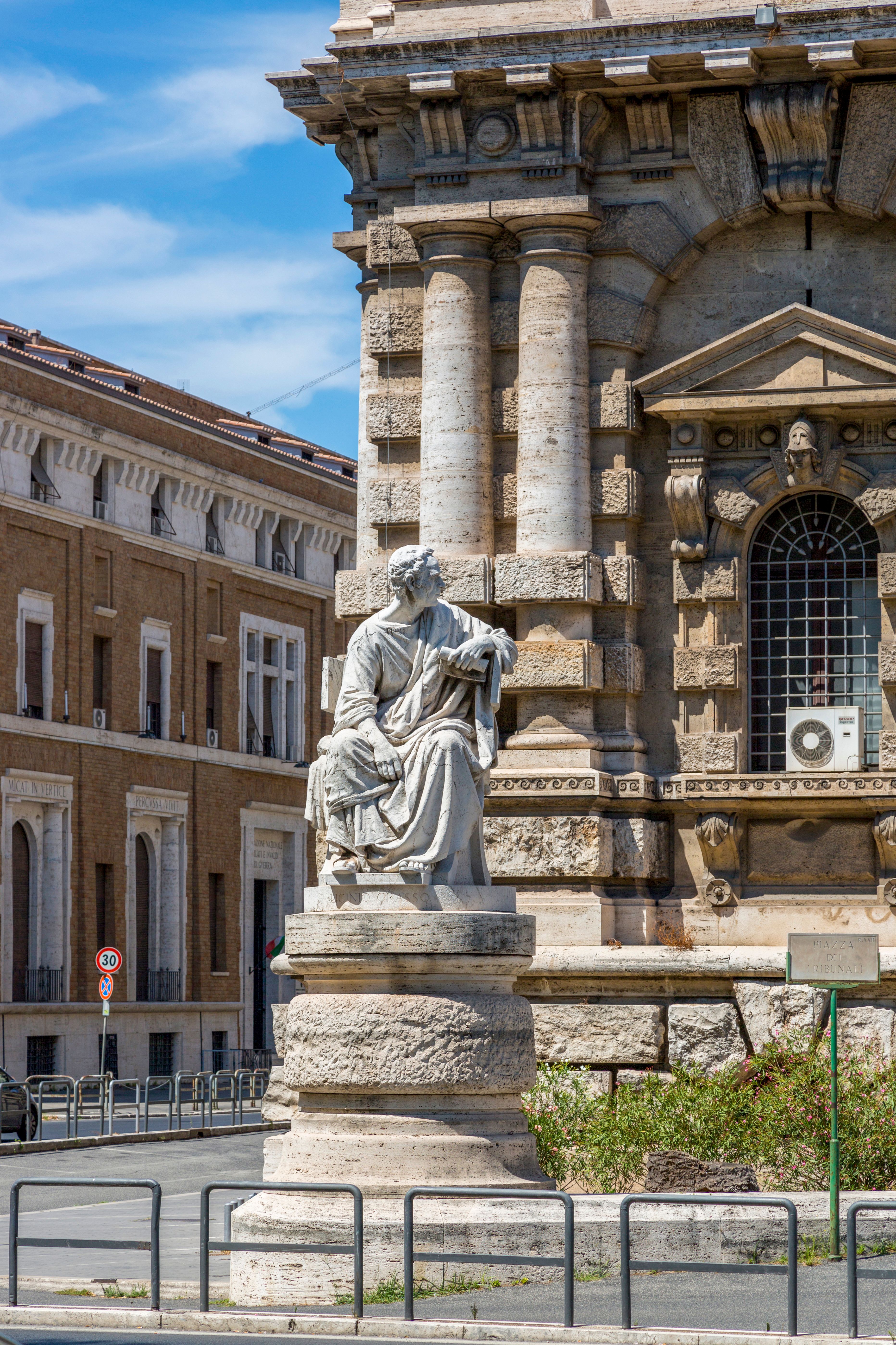 Elegant marble statue near historic European building facade under a clear blue sky.