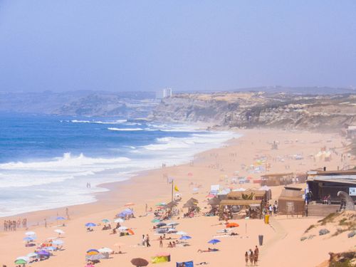 Free Sun-drenched beach in Peniche, Portugal, with colorful umbrellas and seaside cliffs. Stock Photo