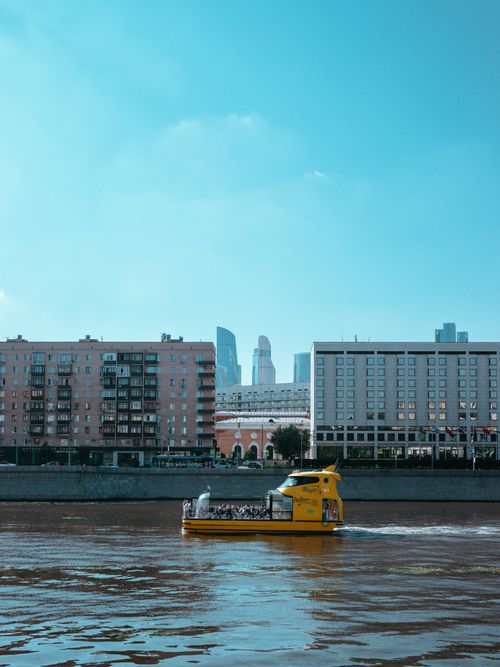 Free Vibrant yellow boat traverses city river with modern skyline backdrop. Stock Photo