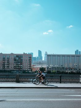 Two cyclists riding through a sunny city with modern buildings in the background.