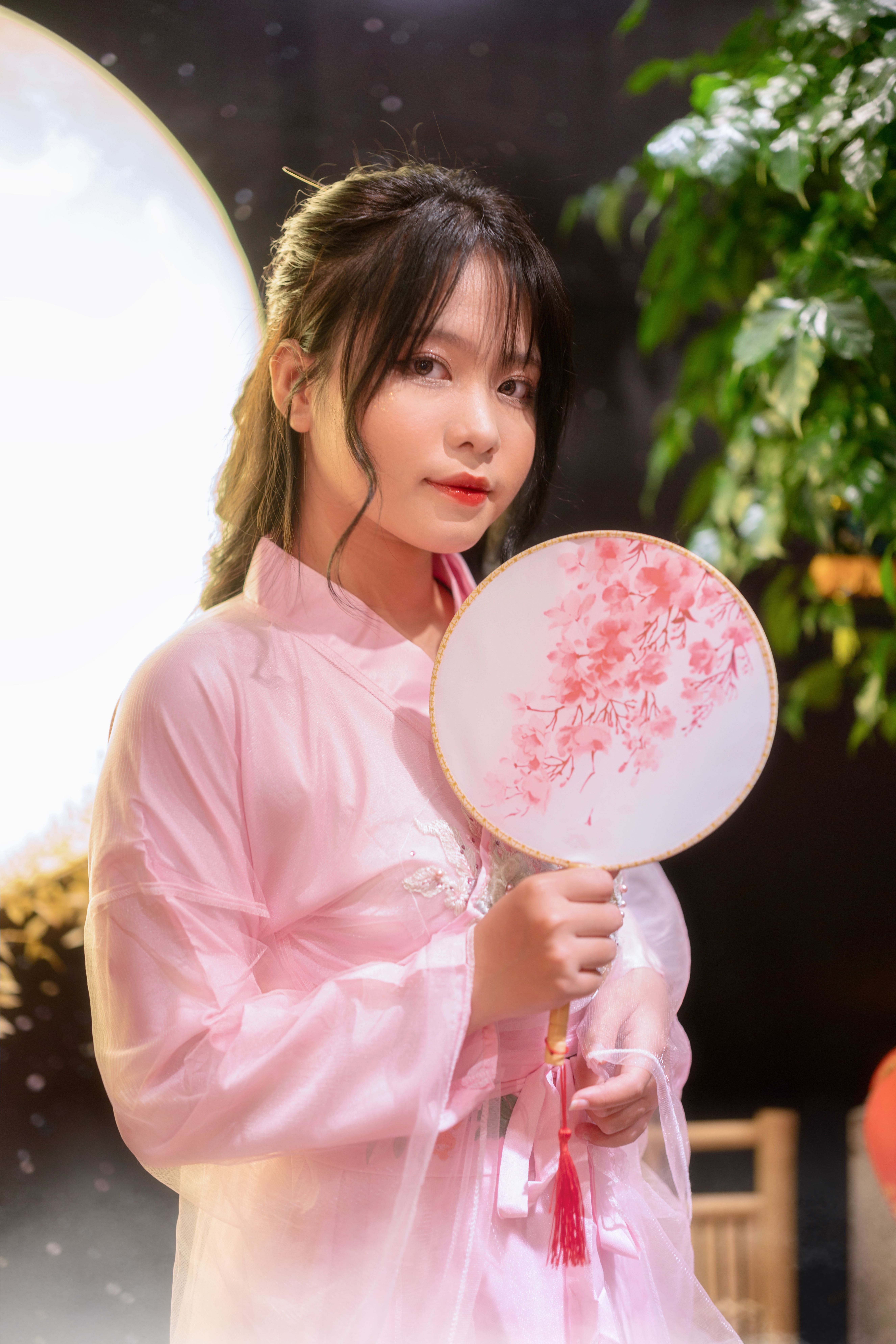 Elegant portrait of a young woman in traditional dress holding a fan indoors.