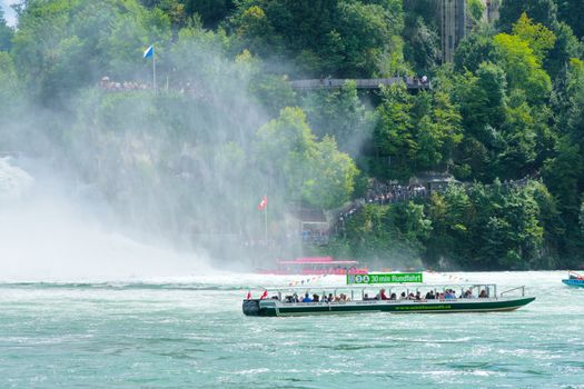 Tour boat cruising near the stunning Rhine Falls in Switzerland, captivating summer scene.