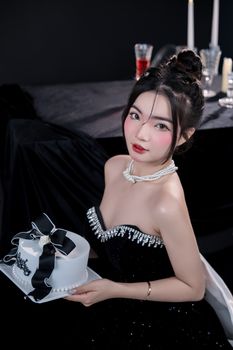 Young woman in elegant attire holding a black and white cake at a celebration.