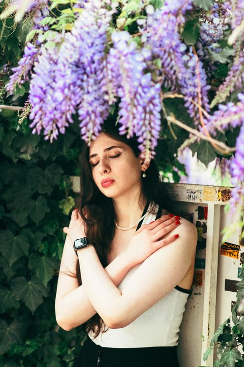 Free Peaceful outdoor portrait of a woman under blooming wisteria, eyes closed in calmness. Stock Photo