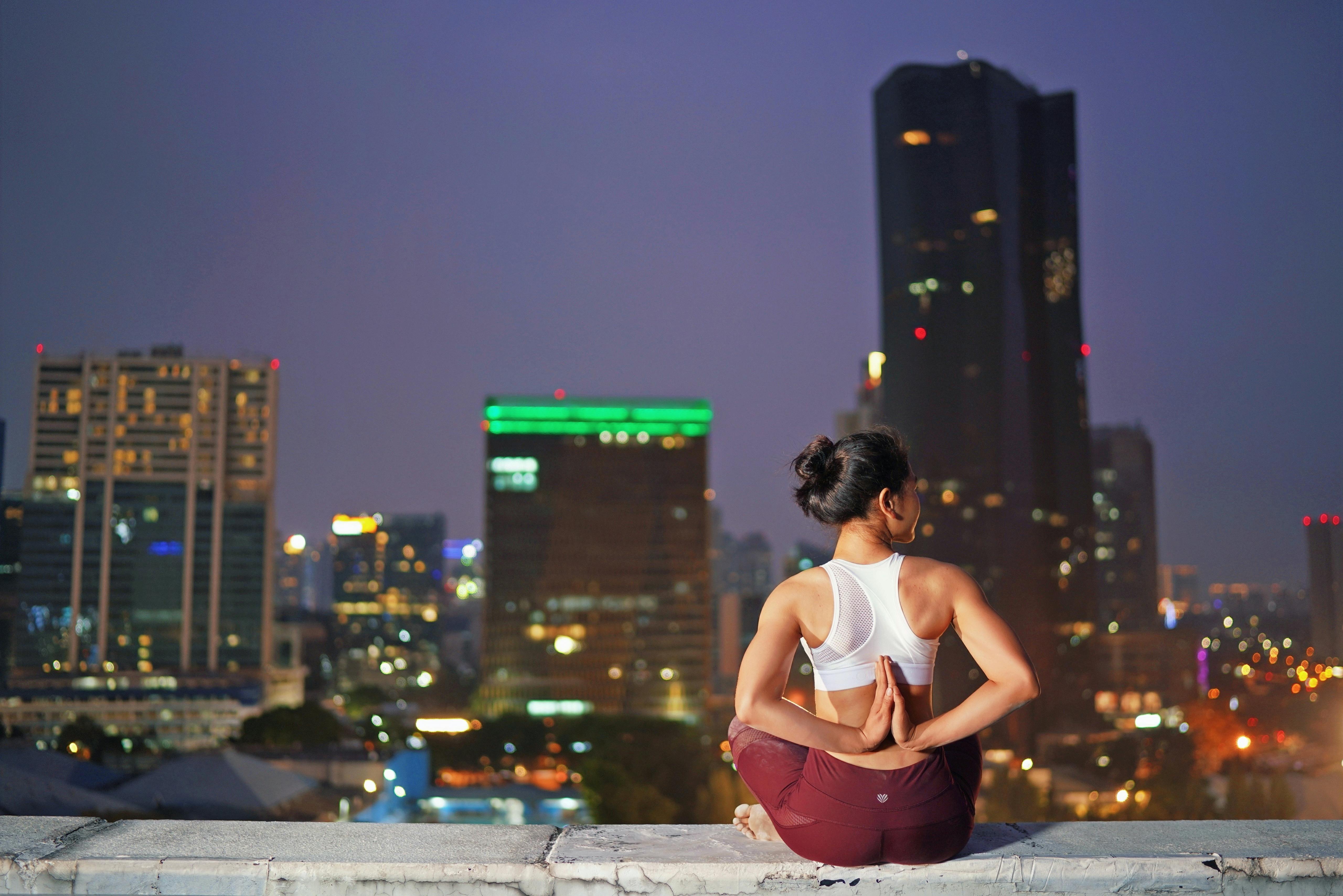 A woman doing yoga on a rooftop with a cityscape backdrop at night, promoting relaxation.
