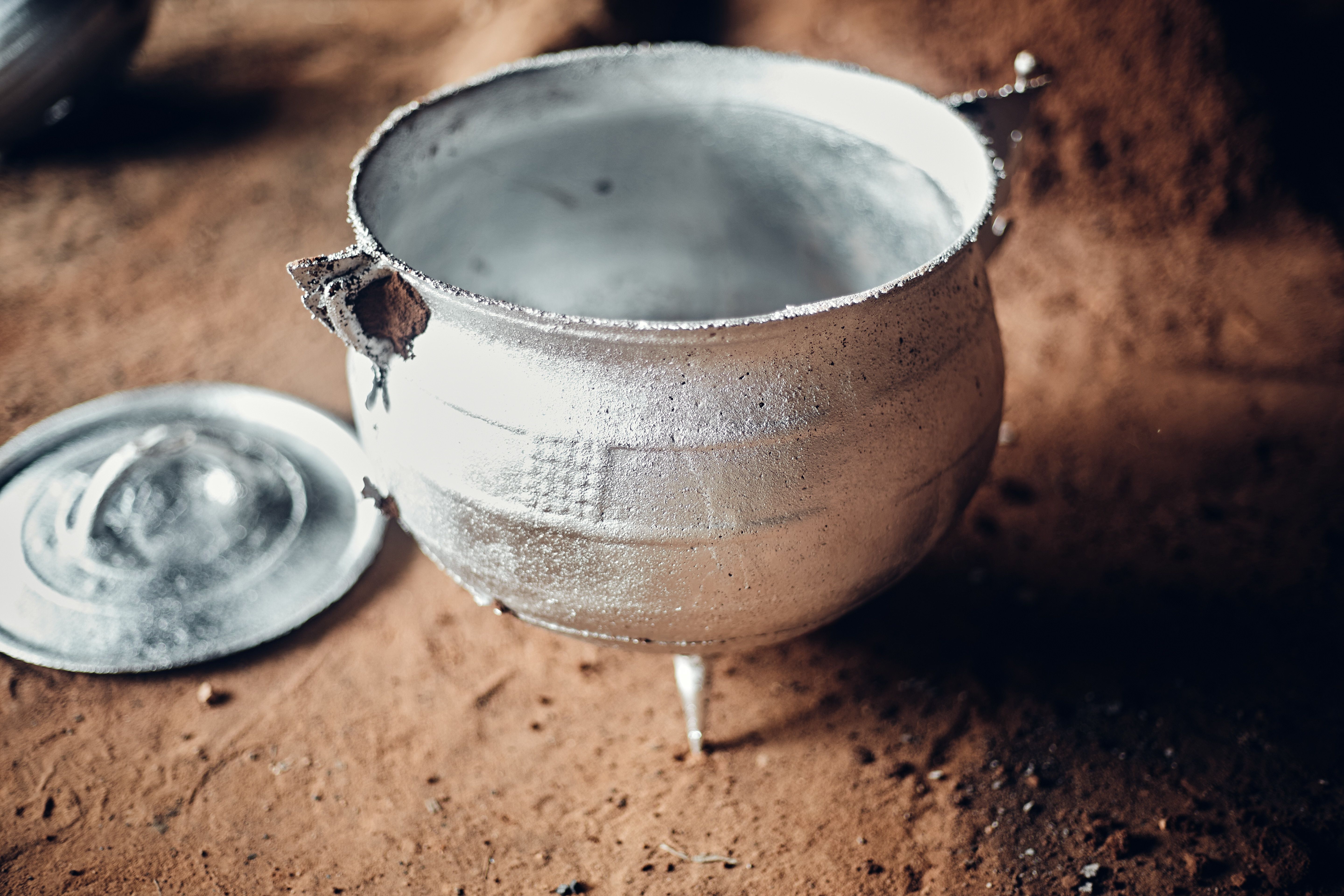 A rustic metal cauldron with a lid on a textured surface, emphasizing vintage style.