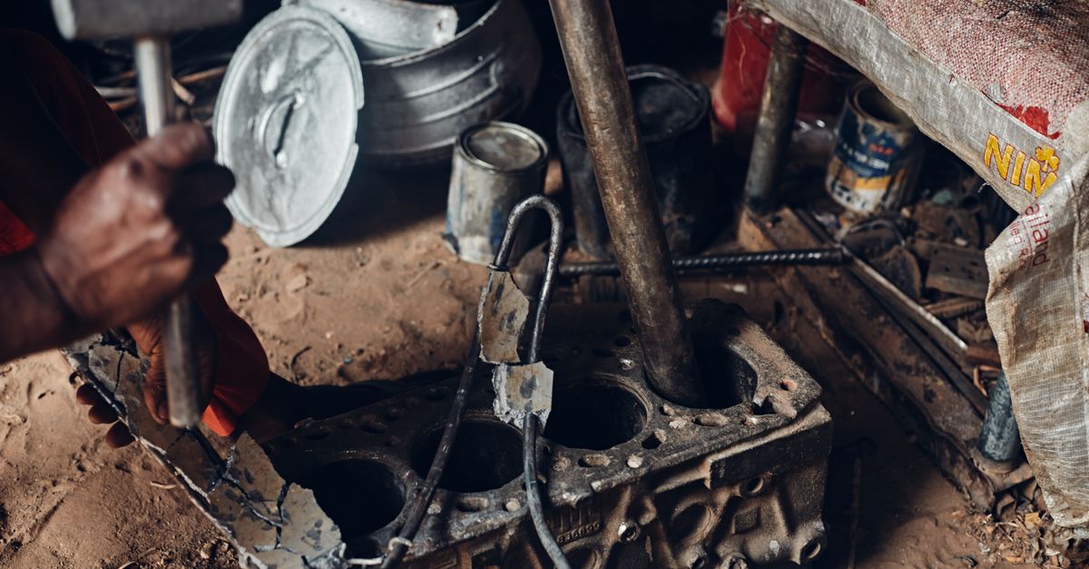 Mechanic working with a hammer on an engine block in a rustic workshop setting.