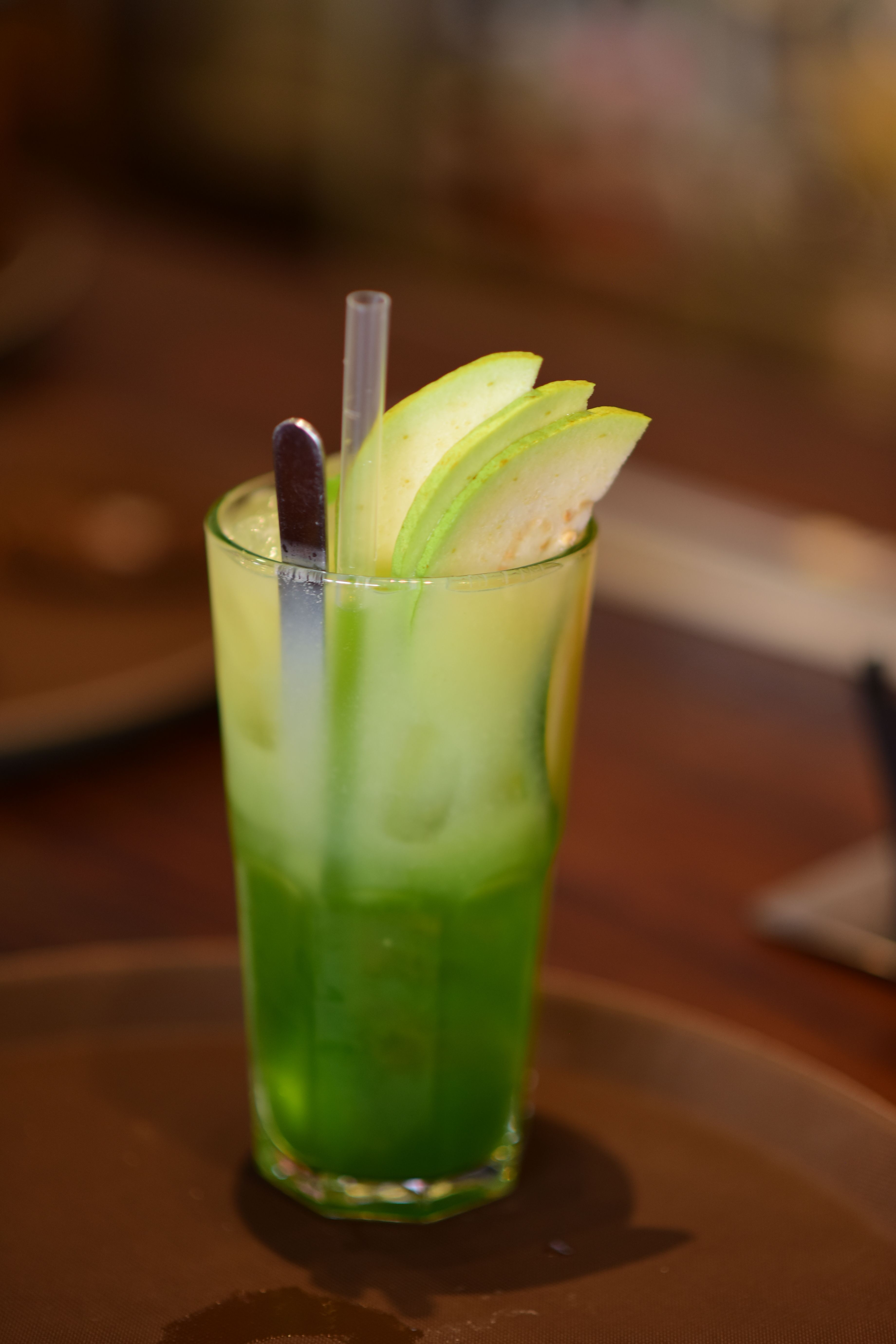 A tall glass filled with vibrant green apple juice garnished with apple slices.