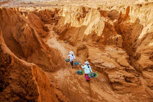 Two farmers carrying baskets through the striking red dunes of Bình Thuận, Vietnam.