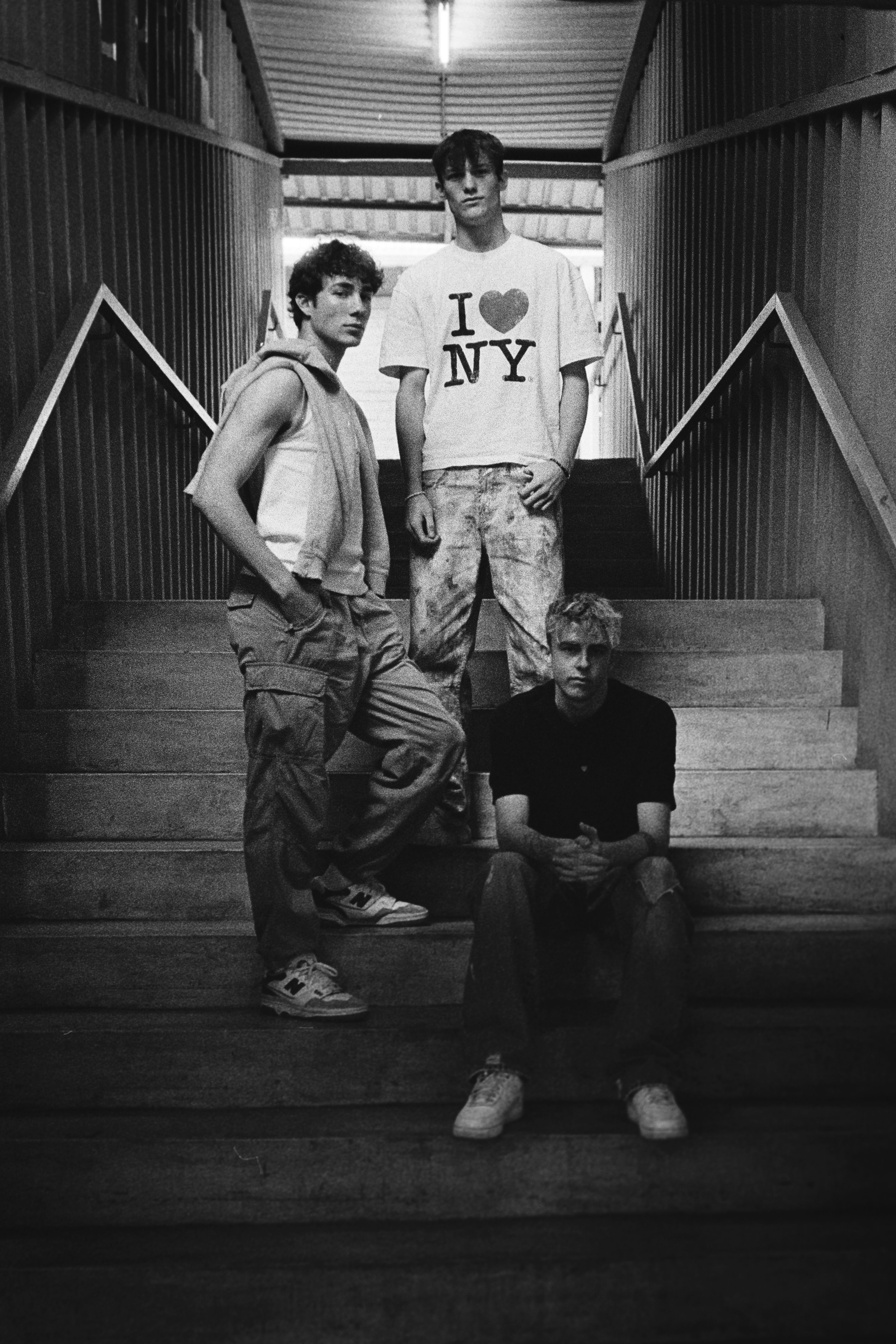A black and white portrait of three young men posing on a concrete stairway in an urban setting.