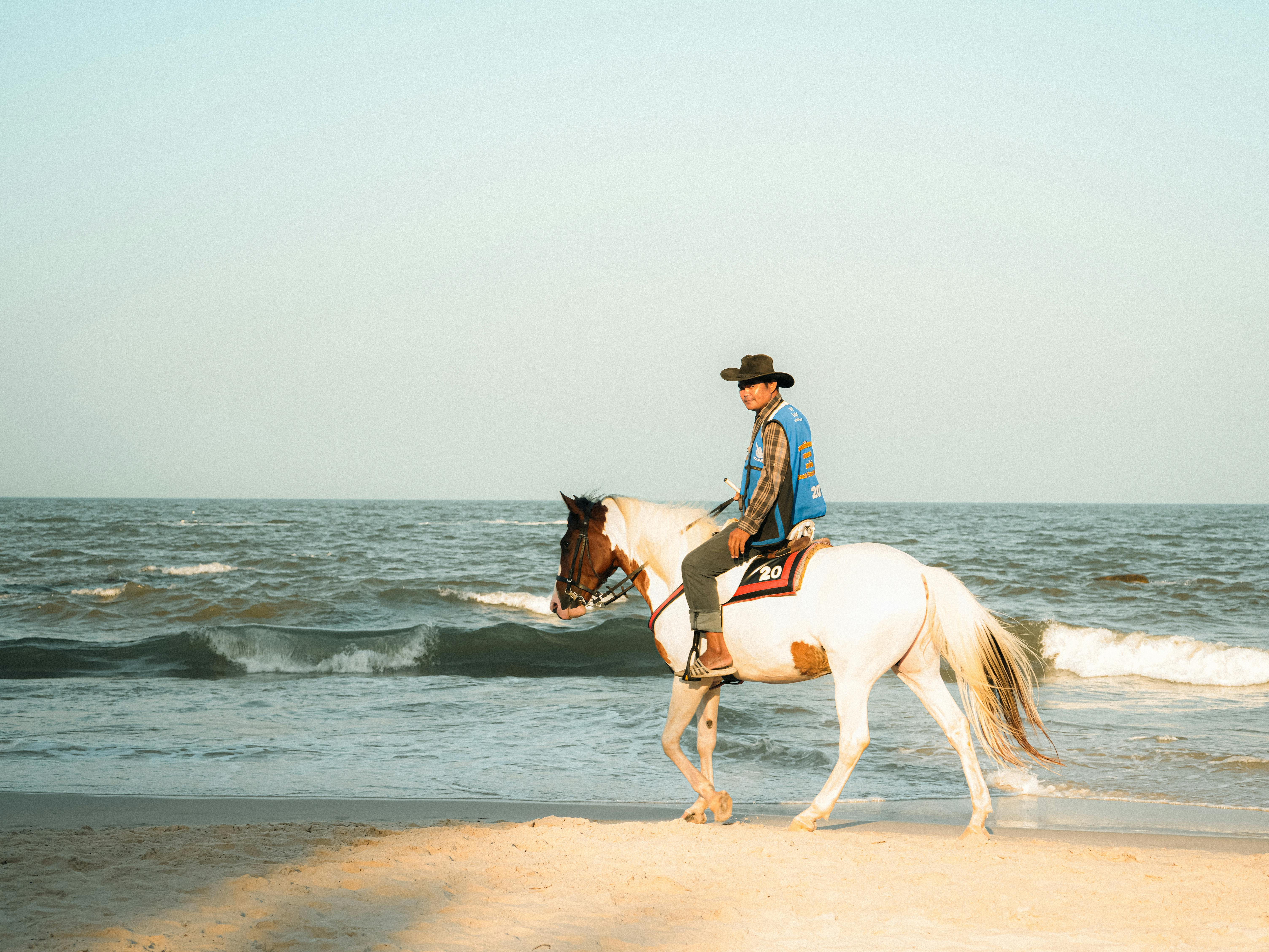 Free A man rides a horse along the beach in Thailand at sunrise, showcasing serene ocean views. Stock Photo