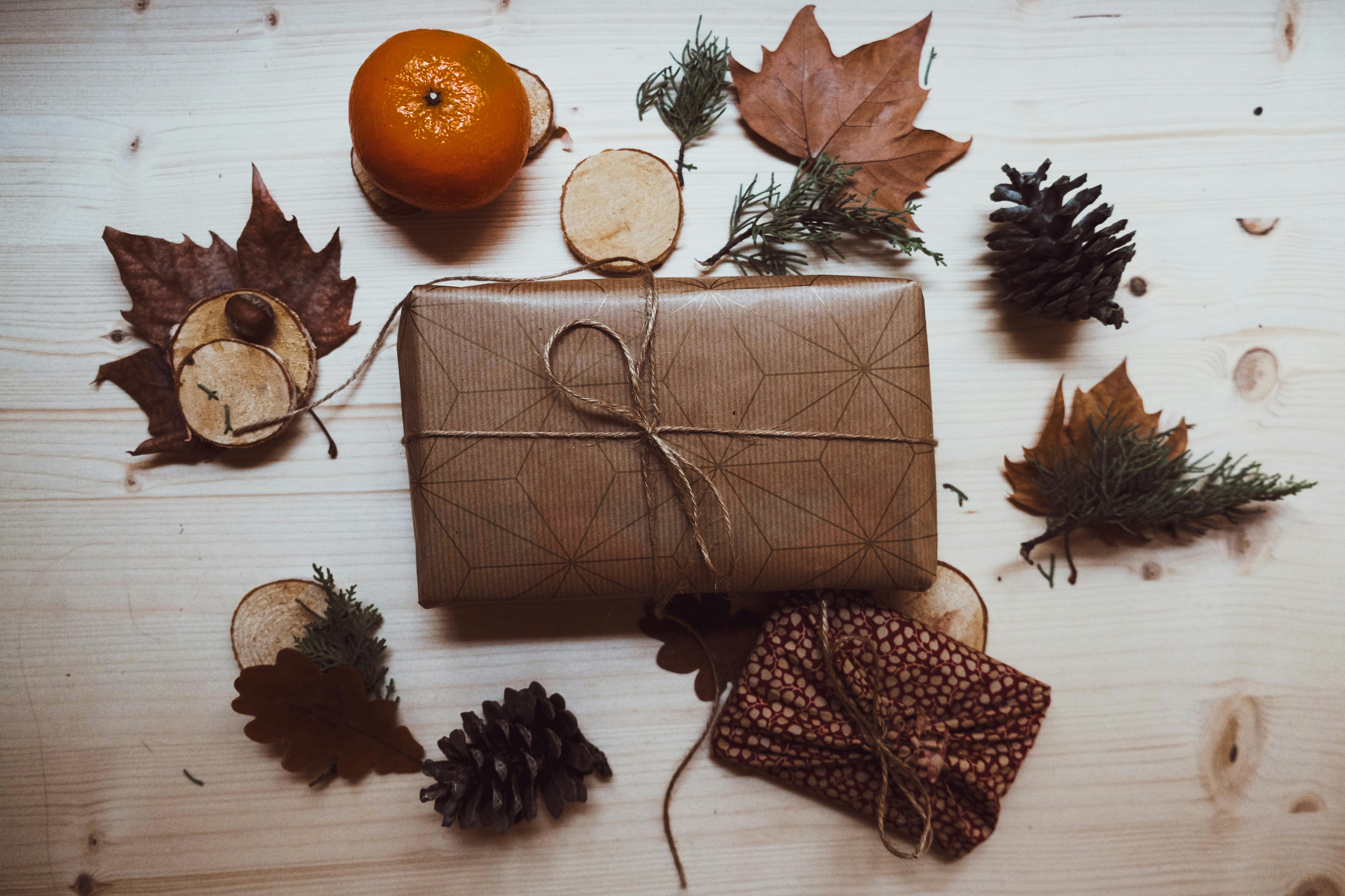 A rustic styled gift wrap with natural autumn elements like pine cones and leaves on a wooden surface.