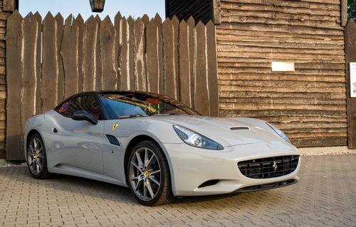 Free Sleek white Ferrari California parked outdoors against a rustic wooden fence on a sunny day. Stock Photo