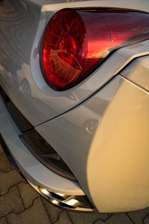 Free Detailed shot of a Ferrari's tail light reflecting sunlight on an outdoor pavement. Stock Photo
