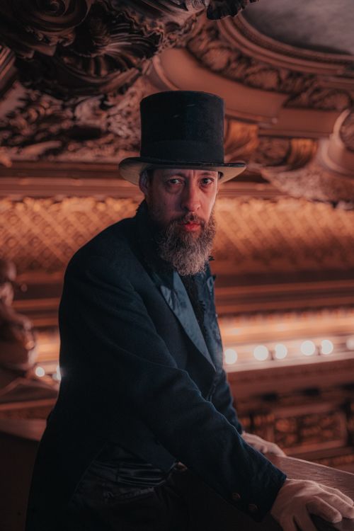 Free Portrait of a gentleman in a top hat inside a grand theater, evoking a historical atmosphere. Stock Photo