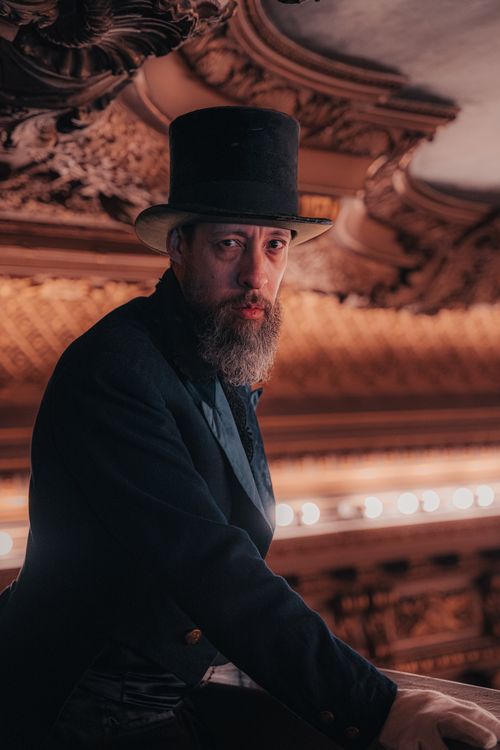 Free Bearded man in top hat and coat inside a lavish, ornate hall capturing Victorian elegance. Stock Photo