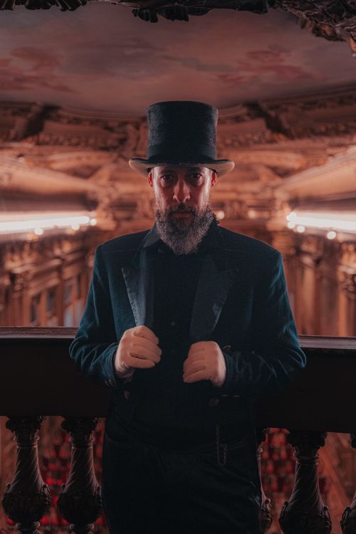 Free Man in vintage costume and top hat stands in opulent hall with intricate decor, capturing a sense of historical elegance. Stock Photo