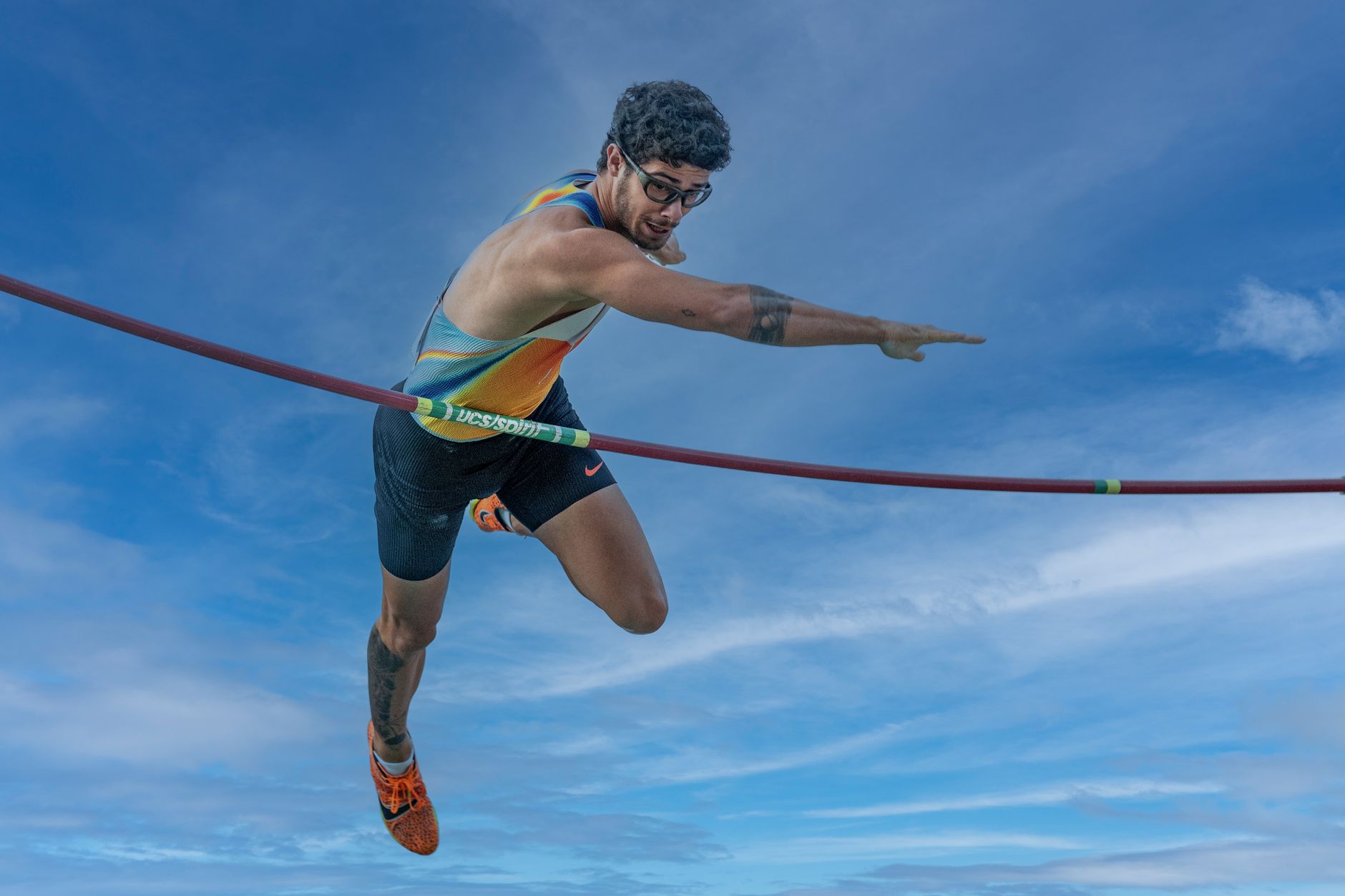 High-energy capture of a pole vaulter in action against a vibrant sky.
