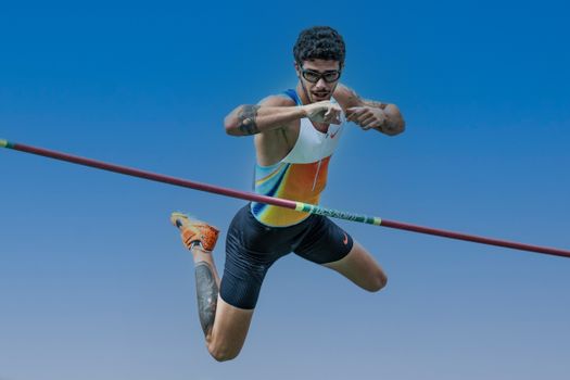 Athlete performing a pole vault jump, showcasing skill and athleticism against a clear blue sky.