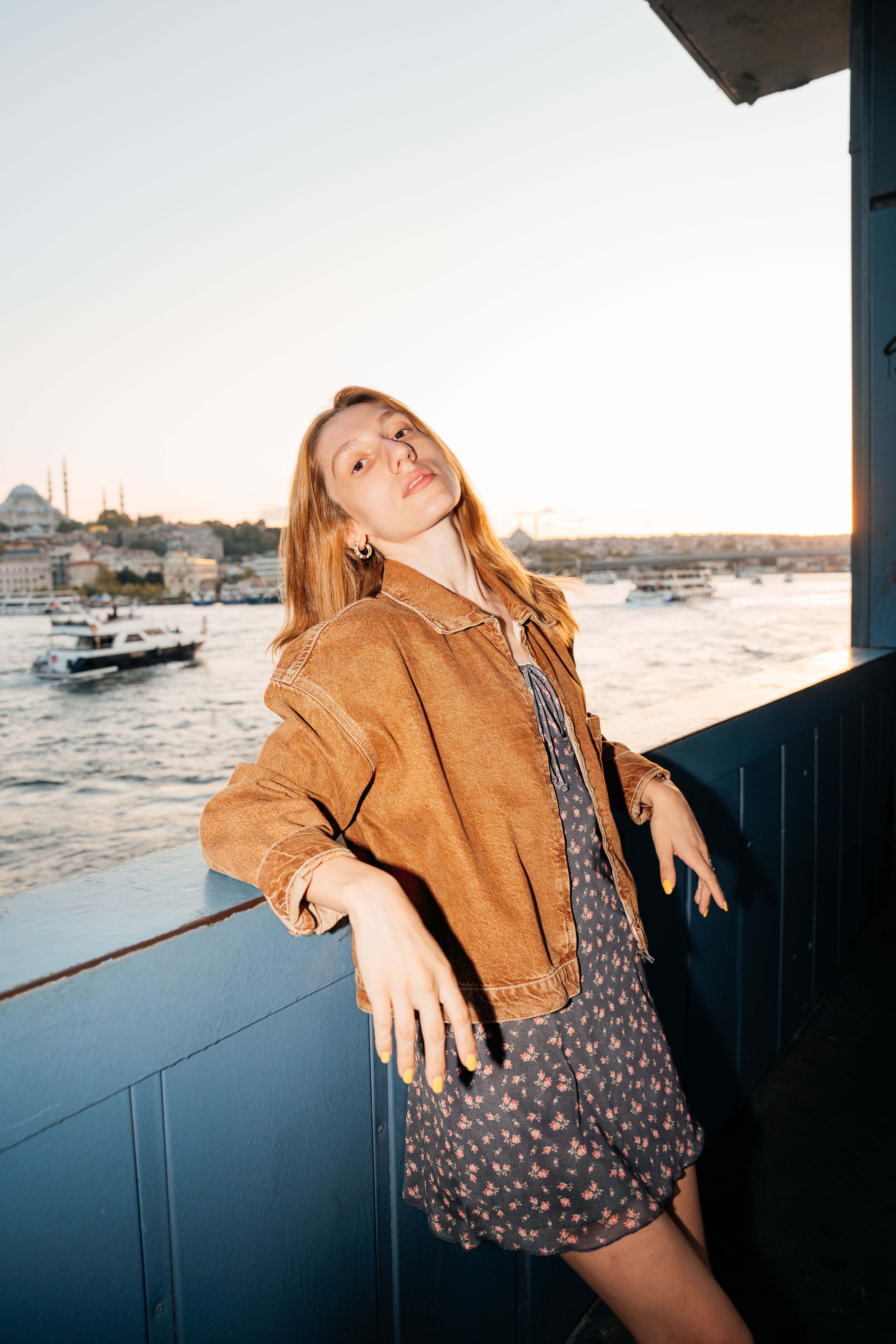 Woman poses by the Bosphorus in Istanbul as the sun sets, blending fashion with iconic skyline views.