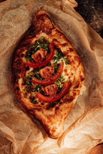 Delicious homemade Georgian khachapuri bread topped with tomatoes and herbs on parchment.