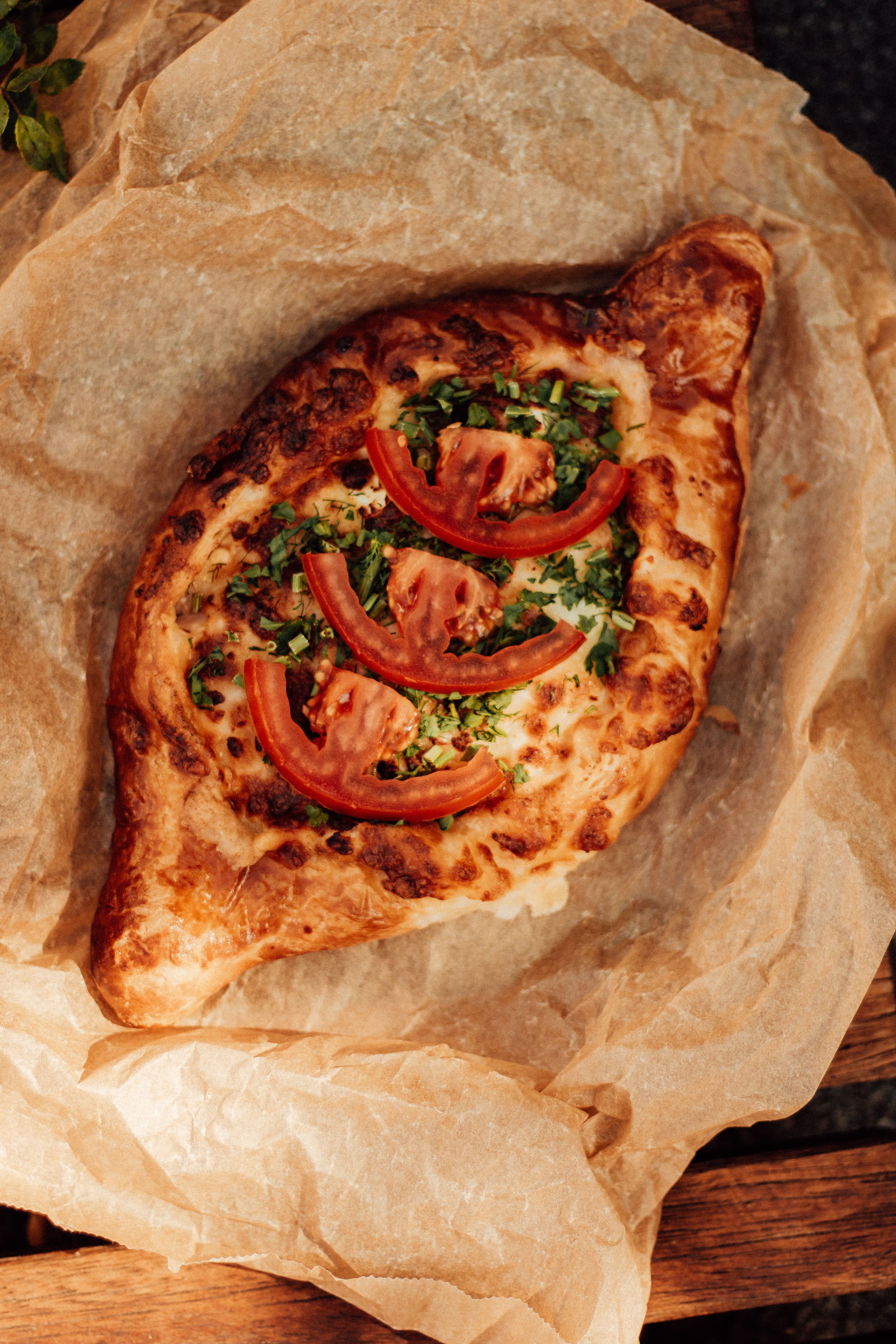 Freshly baked Georgian Khachapuri topped with tomatoes and herbs on parchment paper.