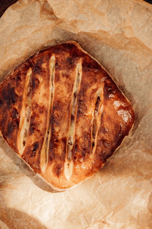 Free Top view of freshly baked rustic bread with golden crust on parchment paper, perfect for culinary themes. Stock Photo