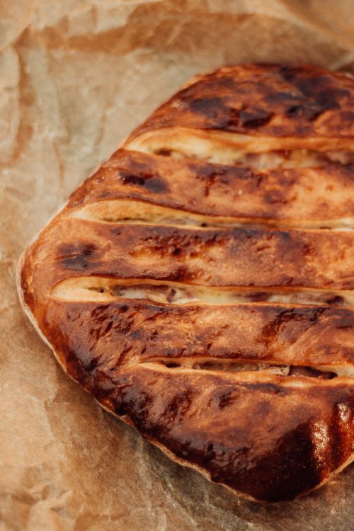 Free Golden-brown homemade rustic bread on parchment paper, highlighting artisanal baking. Stock Photo